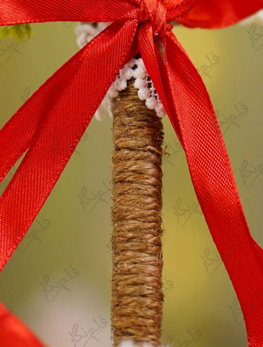 Detailed close up of the red ribbon bow and white lace over the jute-wrapped handle
